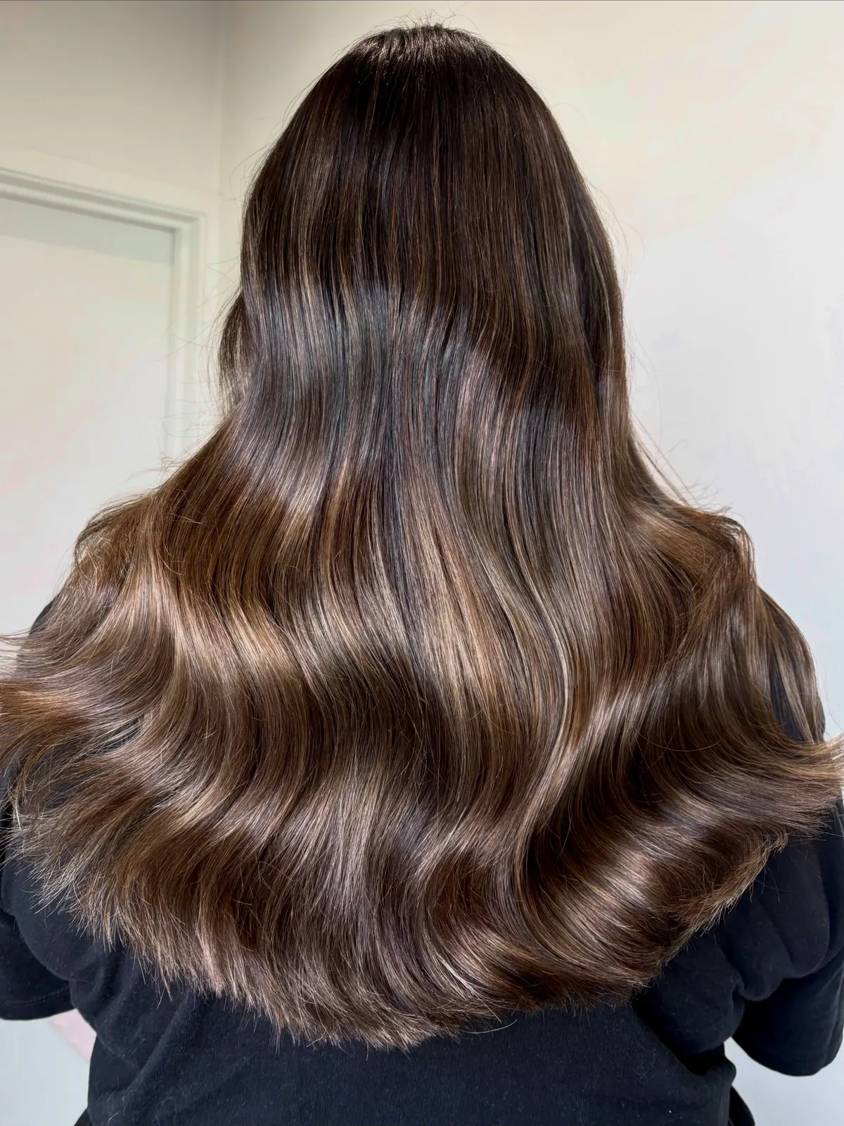 Long dark brunette hair from behind, finished in broad, glossy waves with soft lighter tones through the lengths